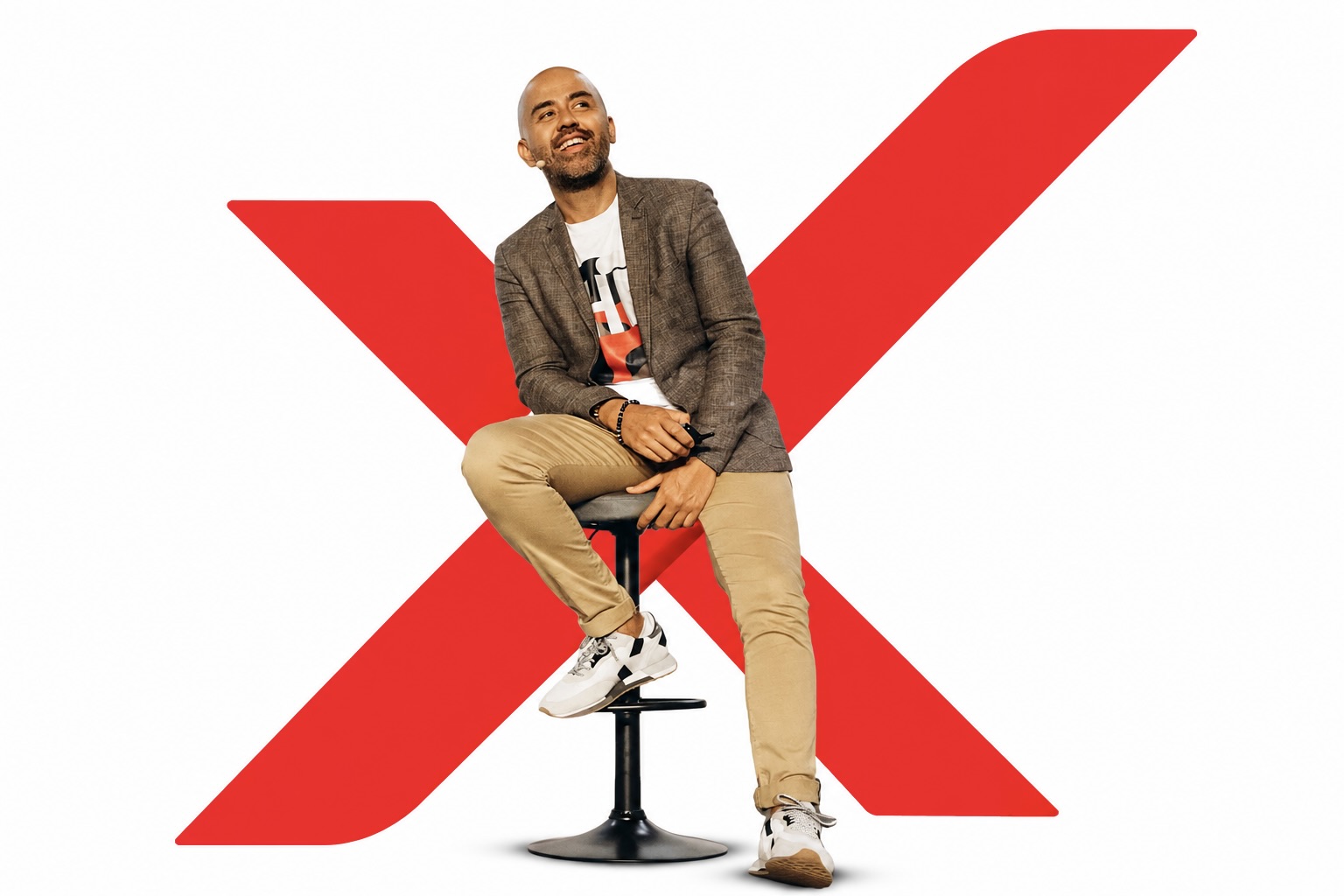 Yannick Alain souriant sur son tabouret, devant le grand X rouge XPANSION.